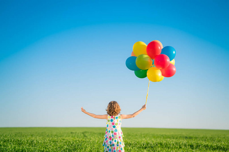 快乐的孩子在户外玩明亮的多色气球。 在蓝天背景下在绿色春天的田野里玩得很开心。 健康积极的生活方式观念。 后视镜