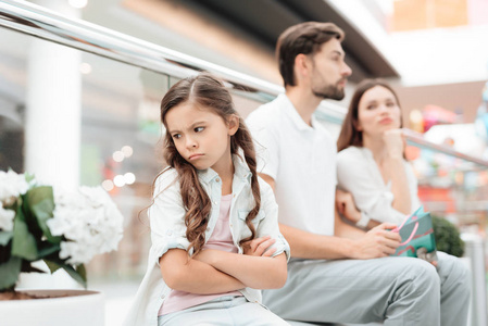 家人父亲母女都坐在商场的长椅上。女孩是愤怒和悲伤