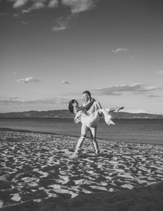 男人背着女人穿白色连衣裙, 夫妻俩在假期快乐。情侣在海滩上, 海边的爱情站。情侣相爱的乐趣, 海和地平线背景。蜜月, 婚礼, 刚