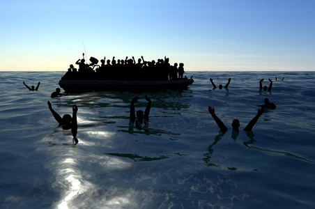 难民在大海中央的一艘大橡皮艇上，需要帮助。 大海里有人在水里寻求帮助。 穿越海洋的移民
