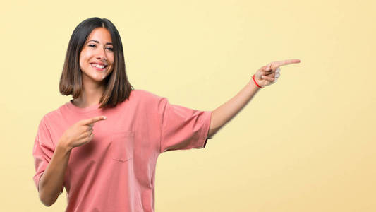 年轻的女孩，粉红色衬衫，手指指向一边，呈现一个产品，同时微笑在黄色的背景。