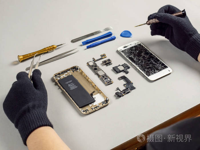 技师或工程师拆卸损坏的智能手机部件,以修理或更换办公桌上的新部件