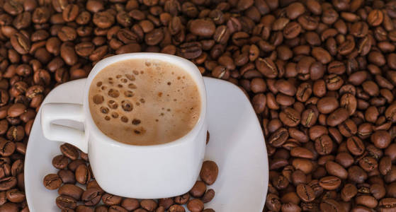 在咖啡豆的背景上，用热咖啡和泡沫特写白色杯子。选择性聚焦。黄金咖啡。