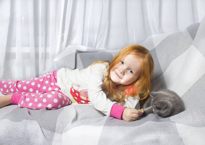 小可爱的女孩在家里沙发上和小猫玩。 生活方式儿童照片。