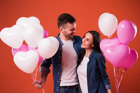 年轻漂亮的情侣在休闲装中与五颜六色的气球一起摆姿势。 情人节假期