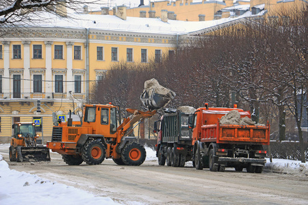 在冬天的城市街道上，一辆拖拉机把街上的雪卸成大卡车