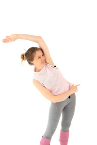 微笑的年轻金发女孩穿着粉红色的紧身裤，穿着灰色的紧身衣，做瑜伽运动体操。 白色背景