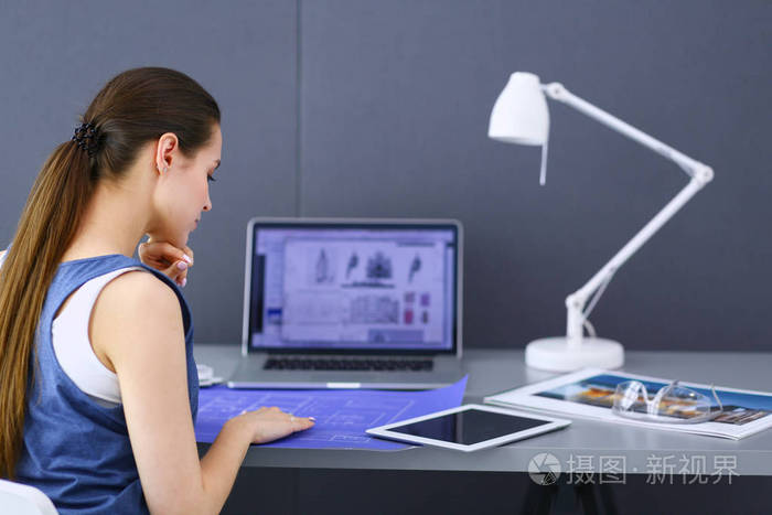 年轻的女人坐在办公桌前与文书计划和笔记本电脑