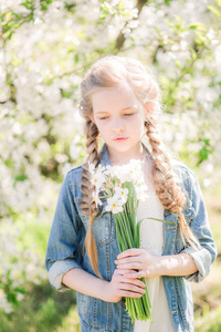 春天，一个金发碧眼的可爱女孩在一个郁郁葱葱的花园里，穿着白色的太阳裙