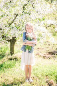 春天，一个金发碧眼的可爱女孩在一个郁郁葱葱的花园里，穿着白色的太阳裙