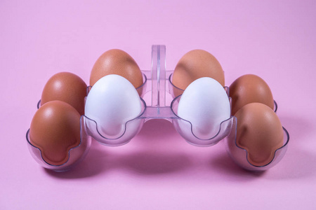 粉红色背景的塑料包装中的白色和棕色鸡蛋