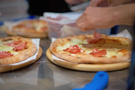 厨师做一个帕玛或意大利火腿披萨，在近距离观看他的手放置肉。 选择性聚焦。