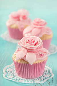 蓝色木制背景上有粉红色花的纸杯蛋糕