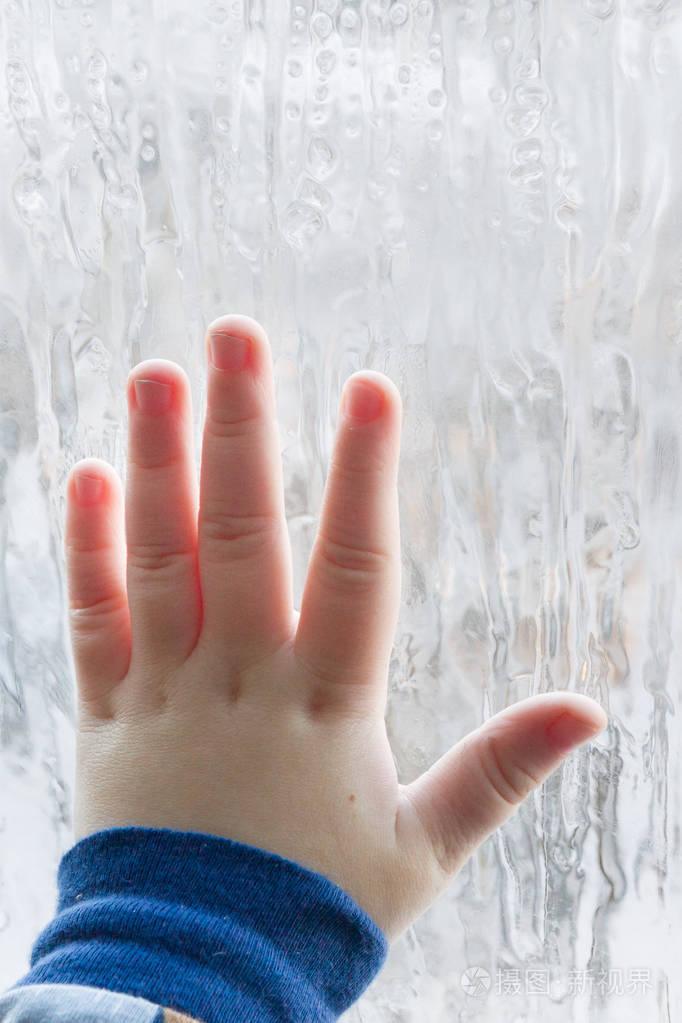 孩子把手掌靠在寒冷的冬天的窗户上