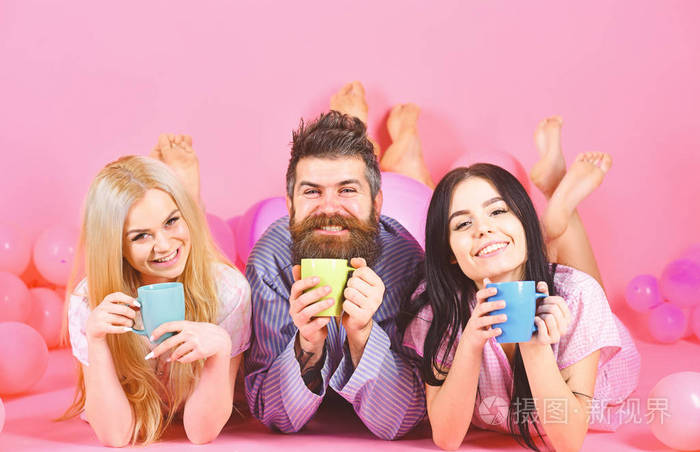 三人早上用咖啡放松 暴风雨夜的概念 男人和女人 朋友在笑脸上躺着 粉红色的背景 恋人在床上喝咖啡 男人和女人在家庭衣服 睡照片 正版商用图片17ixom 摄图新视界