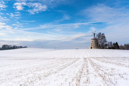 阳光明媚的冬日，空旷的乡村景观，积雪覆盖地面，背景是有趣和快乐的大废弃风车