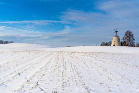 阳光明媚的冬日，空旷的乡村景观，积雪覆盖地面，背景是有趣和快乐的大废弃风车