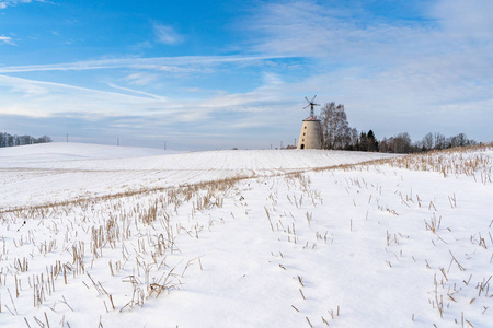 阳光明媚的冬日，空旷的乡村景观，积雪覆盖地面，背景是有趣和快乐的大废弃风车