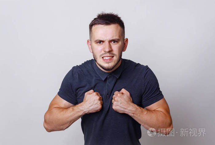 年轻愤怒的肌肉男,咬牙切齿,露出笑容,紧闭的拳头靠近胸部,穿着黑色