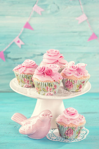 蓝色木制背景上有粉红色花朵的纸杯蛋糕