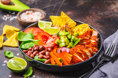 墨西哥鸡肉墨西哥卷碗与米豆，番茄，鳄梨和菠菜黑暗的背景。 墨西哥美食食品概念。