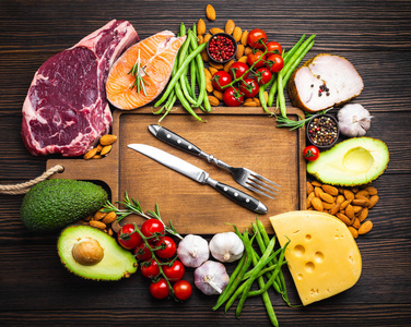 刀叉上的木切割板和生酮低碳水化合物成分的健康饮食概念和减肥的顶部视图。 酮类食物肉鱼鳄梨奶酪蔬菜坚果