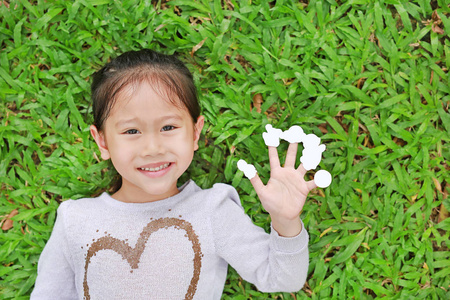 微笑的亚洲小女孩躺在绿草地上，手指上贴着空的白色贴纸。