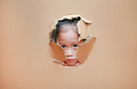 可爱的亚洲小女孩透过洞在纸板上。