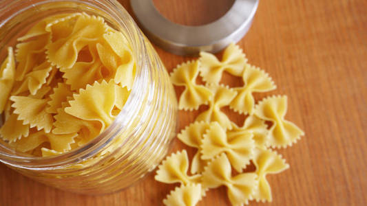 意大利面以蝴蝶结的形式散落在玻璃罐子里。 木制背景上的意大利手工面食。