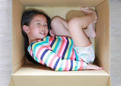 快乐的亚洲小女孩躺在大纸箱里玩耍。