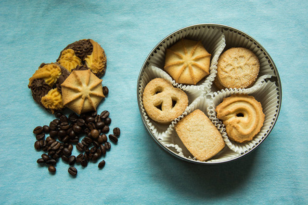 一个圆盒子里有糖的饼干，三个放在浅蓝色桌布上，上面有咖啡豆