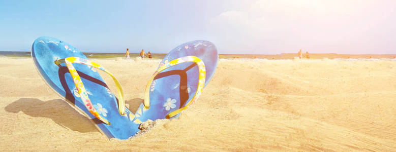 蓝色凉鞋翻盖在白色沙滩上，夏天有蓝色的大海和天空背景
