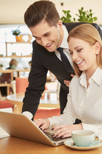 有帮助的伙伴。 一位英俊开朗的商人在餐馆吃午饭时，帮他微笑的女同事拿着笔记本电脑上的文件