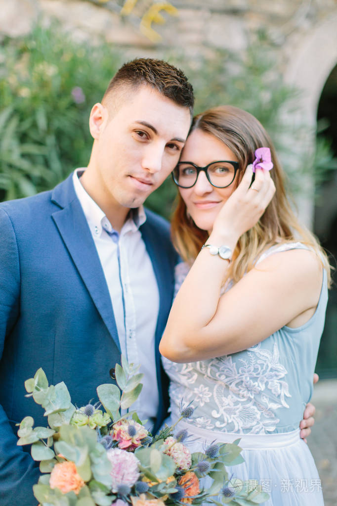 一对年轻漂亮的夫妇穿着蓝色的衣服摆在锡尔米恩中心的房子的正面附近