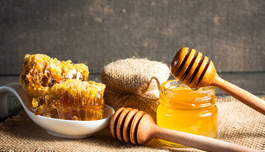 蜂蜜从木制的蜜汁滴在一个罐子里，放在木制的灰色乡村背景上