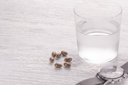 一杯薄雾般的水和棕色的医疗胶囊放在一张白色的旧木桌上。 适当药物和现代食品补充剂的手表图片
