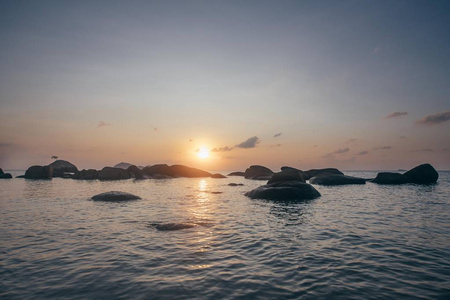海上岩石海岸的日落。 太阳正在离开地平线。 夕阳下的石头和大海