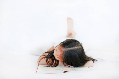 可爱的亚洲小女孩躺在精装书的床上，白色背景。