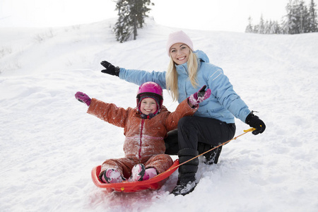 妈妈和女儿骑在雪滑滑梯上的雪橇上。 从雪山骑雪橇。 雪橇骑冬天有趣的雪家庭雪橇。