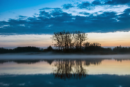 一片平静的湖面上的树木在水中倒影，黄昏的雾和天空中的云