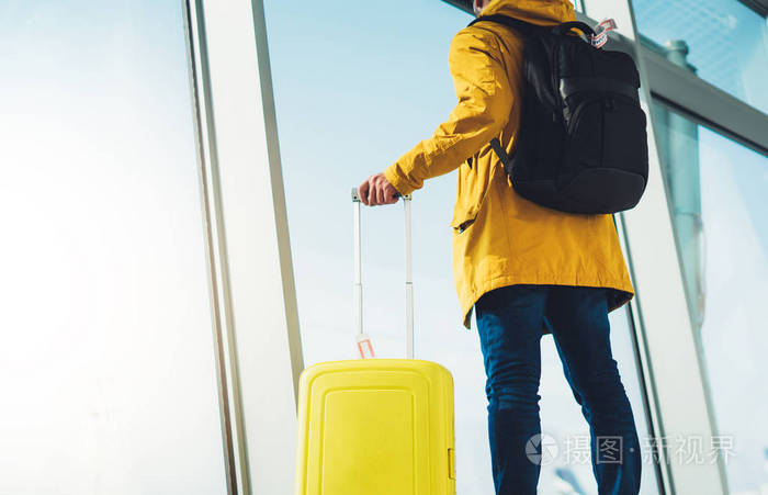 旅客游客带着黄色旅行箱背包站在机场的背景上,大窗户的人穿着明亮的