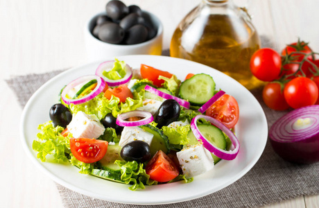 新鲜的希腊沙拉，由樱桃番茄鲁科拉阿古拉法塔橄榄黄瓜洋葱和香料制成。 凯撒沙拉在一个白色的碗在木制的背景。 健康有机