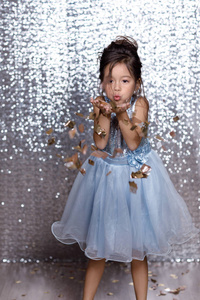 美丽的小女孩在银色和蓝色礼服与五彩纸屑