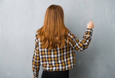 年轻的红头发女孩，用食指指着后面的墙