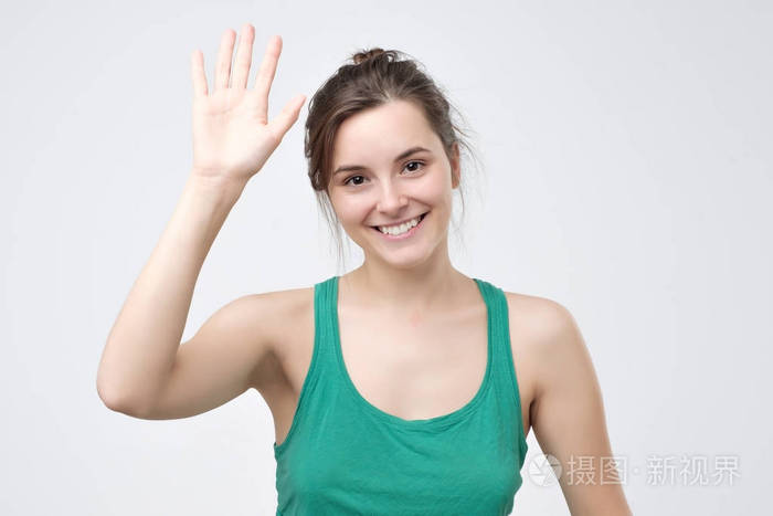 漂亮的学生女孩打招呼,笑得开心,友好地挥动着她的手