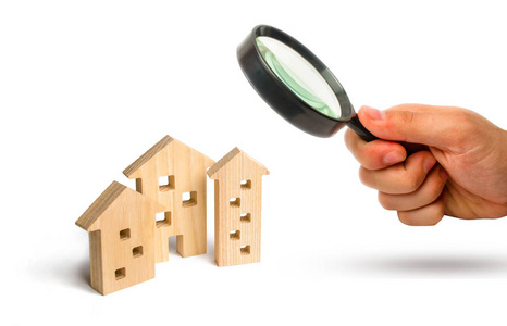 放大镜看着白色背景上的木屋。 房价或租金上涨的概念。 对住房和房地产的需求不断增长。 投资。