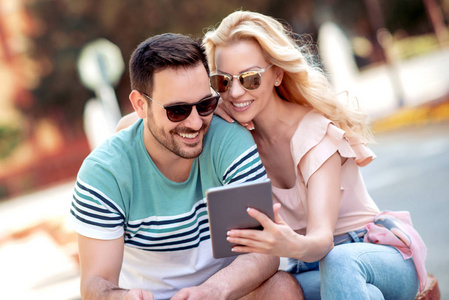 年轻夫妇在夏天喝咖啡，坐在城市公园里，用平板电脑。