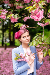 美丽的女孩，粉红色的头发，穿着一件时髦的蓝色裤子，站在五颜六色的花朵旁边。 漂亮的软模型看着相机。