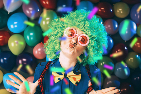 有趣的年轻女子，戴着绿色假发和眼镜，在五颜六色的派对气球背景下摆着几十个气球