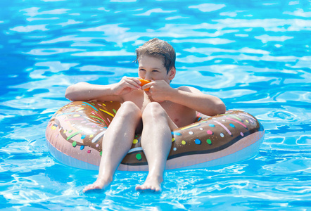 可爱的孩子男孩在有趣的充气甜甜圈浮动戒指在游泳池与橘子。 青少年学习游泳在度假村的户外游泳池里玩得很开心。 给孩子们的水玩具。 
